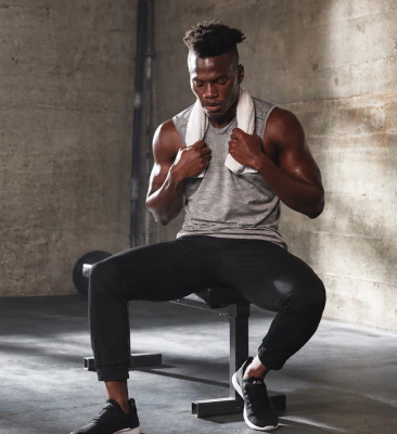 Man resting on a weight bench with a towel around his neck in a concrete gym