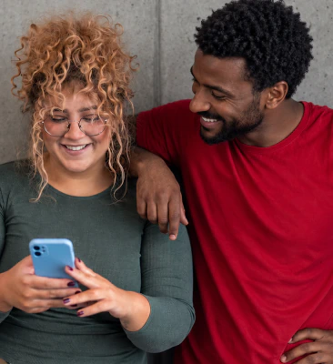 Smiling woman looking at her phone while a man in a red T-shirt leans on her shoulder
